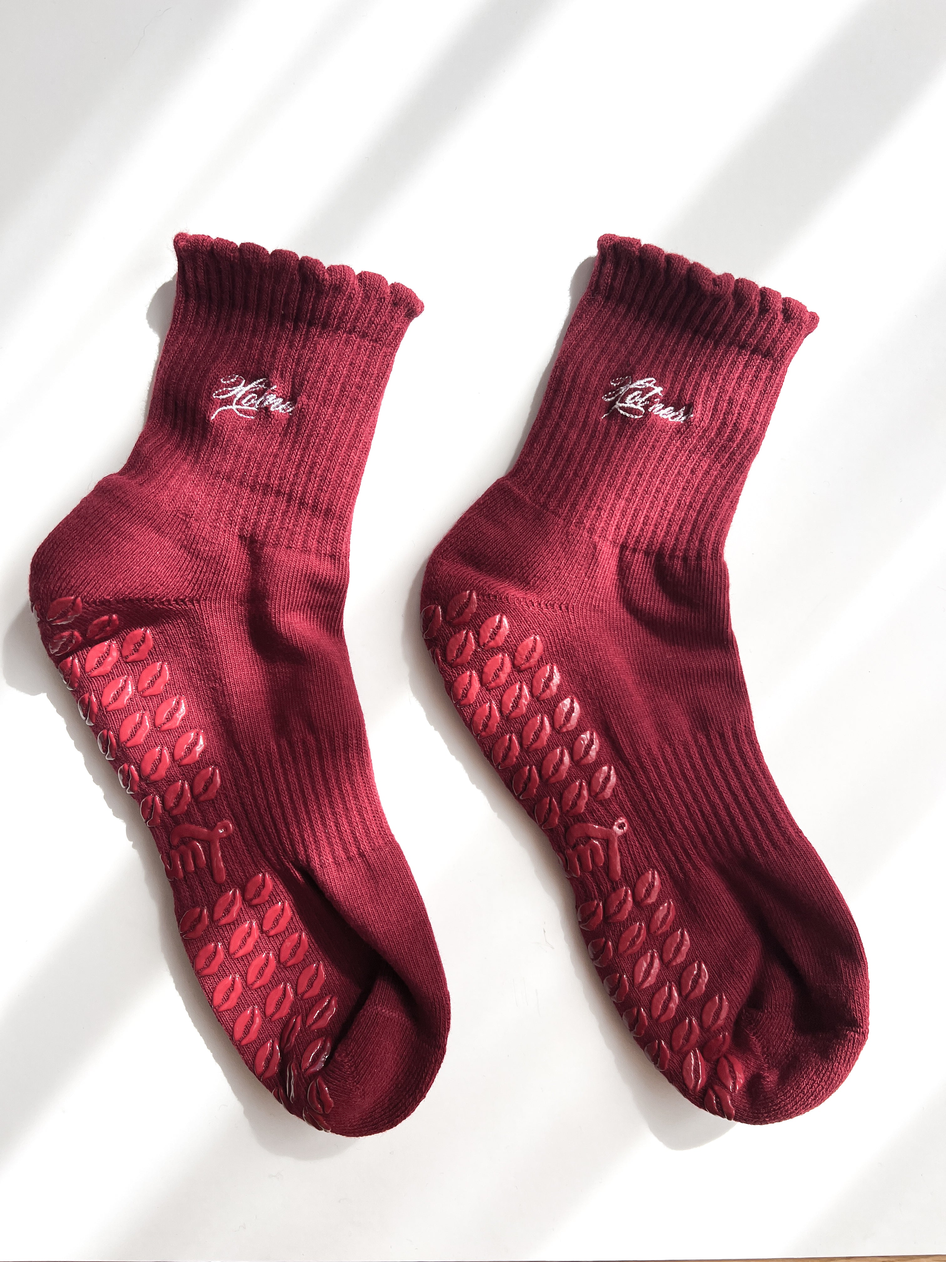 A pair of dark red ankle socks with textured grip patterns on the soles and a small white embroidered text "Hot Mess".