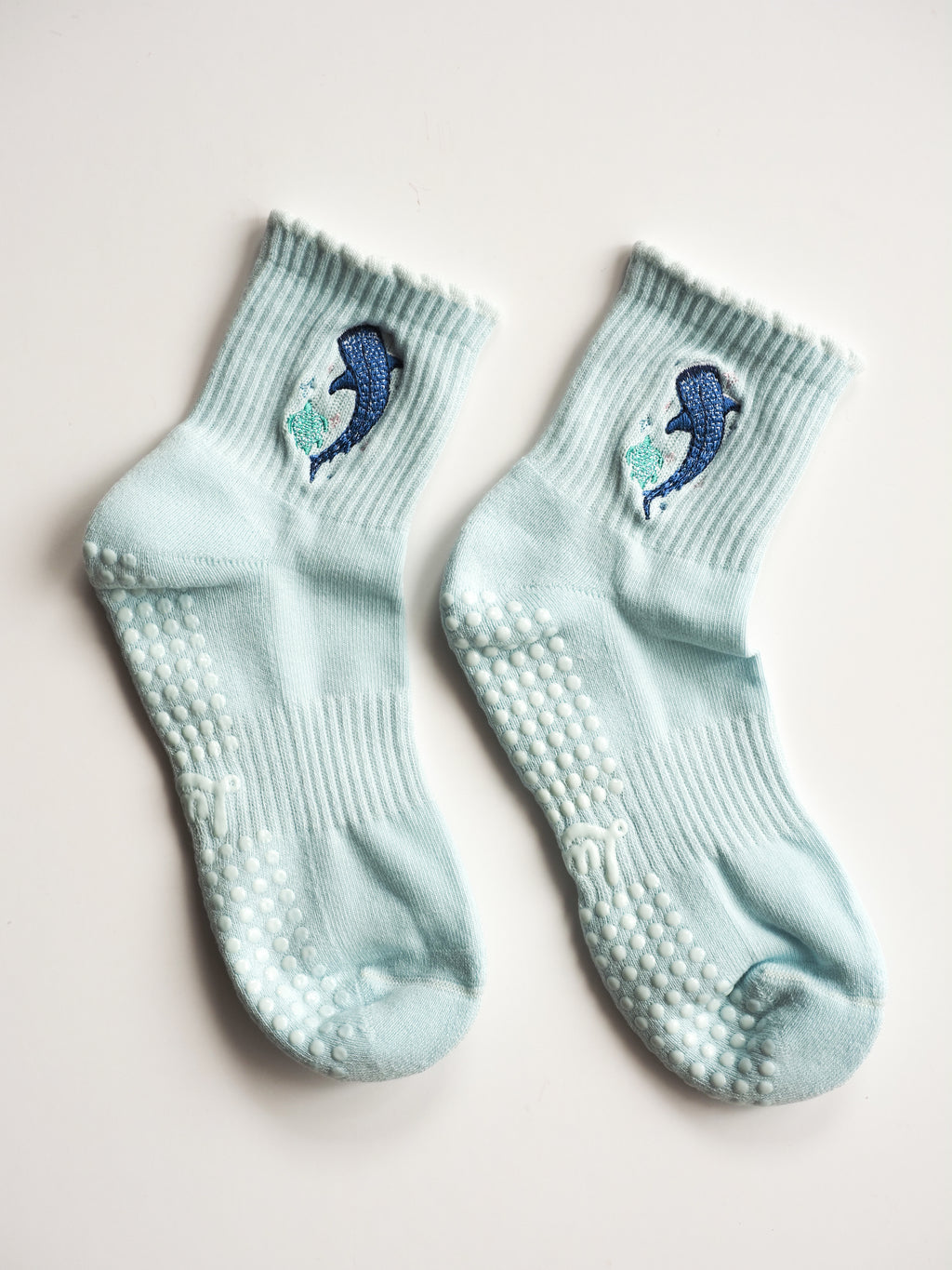 A pair of light blue baby socks with non-slip grip dots on the soles, featuring blue whale and sea turtle embroidery.
