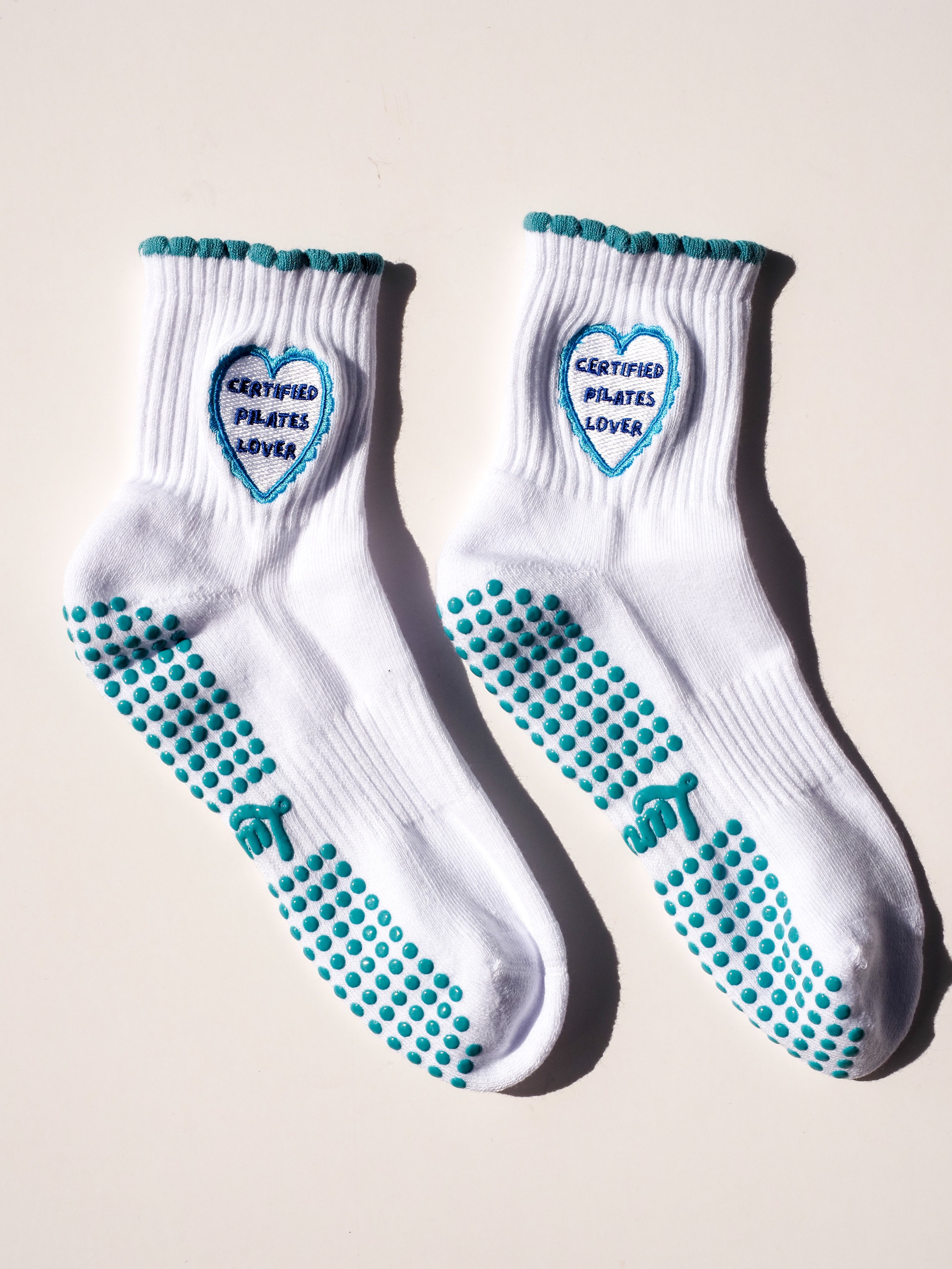 Product shot of white Pilates grip socks with blue accents and the words "Certified Pilates Lover".